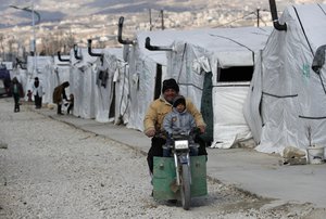 A Syrian displaced man and his son ride a motorcycle, as they drive between the tents at a refugee camp, in Bar Elias, in eastern Lebanon's Bekaa valley, March 5, 2021