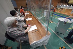 Staff members of a local election administration commission, wearing face masks, observe a voter cast a ballot in the upper house elections at a polling station Sunday, July 10, 2022, in Tokyo.