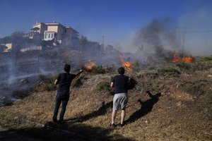 Residents spray water with a hose as fire burns near houses in the area of Drafi east of Athens on Wednesday, July 20, 2022.