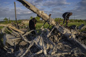 Oleksiy Polyakov, right, and Roman Voitko check the remains of a destroyed Russian helicopter lie in a field in the village of Malaya Rohan, Kharkiv region, Ukraine, Monday, May 16, 2022.