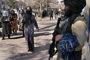 File - Afghan women pass next to a Taliban fighter in Kabul, Afghanistan, Feb. 13, 2022. The lives of Afghan women and girls are being destroyed by the Taliban’s crackdown on their human rights, said Amnesty International in a new report Wednesday, July 27, 2022.