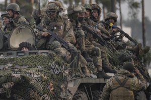 Ukrainian servicemen ride on an armored transporter driving through a Russian position overran by Ukrainian forces as a fellow soldier salutes them outside Kyiv, Ukraine, Thursday, March 31, 2022