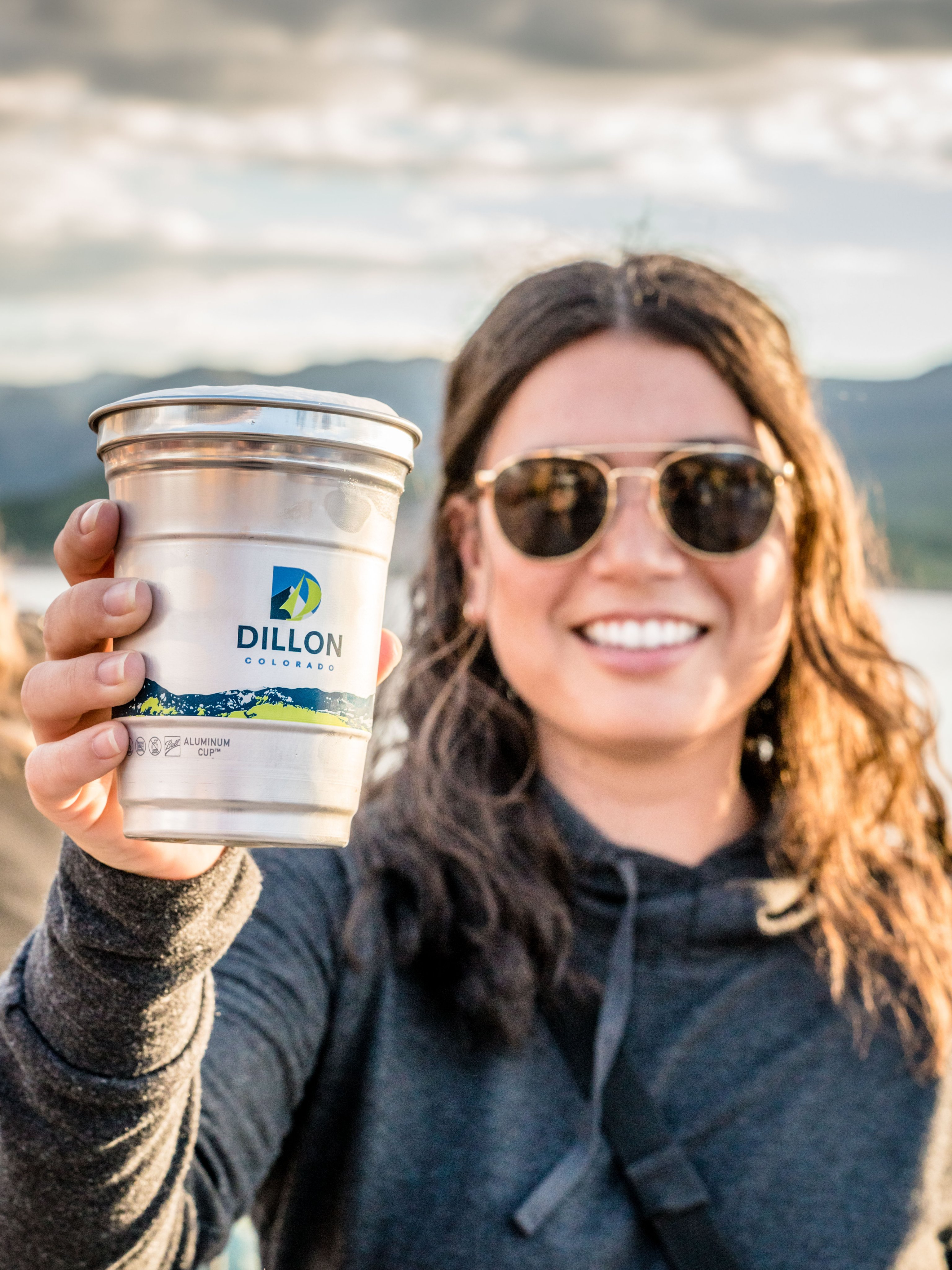 Woman holding a custom designed recyclable Ball Aluminum Cup with the mountains of Dillon, CO behind her.