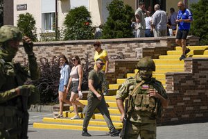 File - People walk past as Russian soldiers guard an office for Russian citizenship applications, in Melitopol, south Ukraine, July 14, 2022. Russia took control of part of the Zaporizhzhia region quickly after the launch of the military operation in Ukraine.