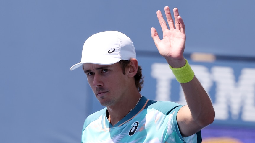 A cap-wearing Alex de Minaur waves at the crowd in acknowledgement after his win at the US Open.