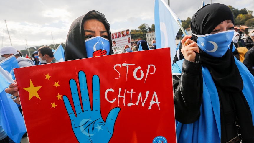 A woman in a headscarf holds a placard reading 'stop China'