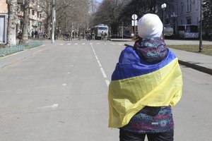 File - A woman covered by Ukrainian flag stands in front of Russian troops in a street during a rally against Russian occupation in Kherson, Ukraine, on March 19, 2022.