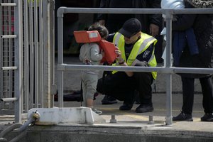 A child is helped to remove a bouyancy aid after arriving with adults thought to be migrants who undertook the crossing from France in small boats and were picked up in the Channel, following their disembarkation from a British border force vessel, in Dover, south east England, Friday, June 17, 2022. The British government vowed Wednesday to organize more flights to deport asylum-seekers from around the world to Rwanda, after a last-minute court judgment grounded the first plane due to take off under the contentious policy.