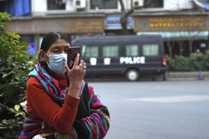 File - A woman in Tibetan garb looks at her cellphone while a police vehicle stands in the background in the Tibetan quarter of Chengdu, in southwestern China's Sichuan province, on Monday, Feb. 7, 2022. Ahead of the Beijing summer Olympics 14 years ago, deadly demonstrations erupted across the Tibetan plateau. But now Tibet has fallen silent, even as the Olympic games come to Beijing for a second time, as many Tibetans resign themselves to increasingly intrusive Chinese rule.