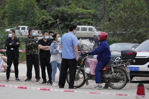 Government workers control access at the entrance to Lv village which leads to the site of the China Eastern plane crash, Tuesday, March 22, 2022, in southwestern China's Guangxi province