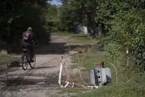 A man cycles past part of a rocket that sits wedged in the ground at a residential area in Sloviansk, Ukraine, Monday, Sept. 5, 2022.