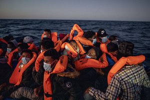 In this Friday, Feb 12, 2021 file photo, a woman holds a 3 month old baby as migrants and refugees from different African nationalities wait for assistance on an overcrowded rubber boat, as aid workers of the Spanish NGO Open Arms approach them in the Mediterranean Sea, international waters, at 122 miles off the Libyan coast