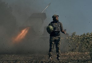 File - A Ukrainian soldier holds a watermelon and thumbs up as a rocket launch system fires in the font line in Donetsk region, eastern Ukraine, Saturday, Aug. 3, 2022.