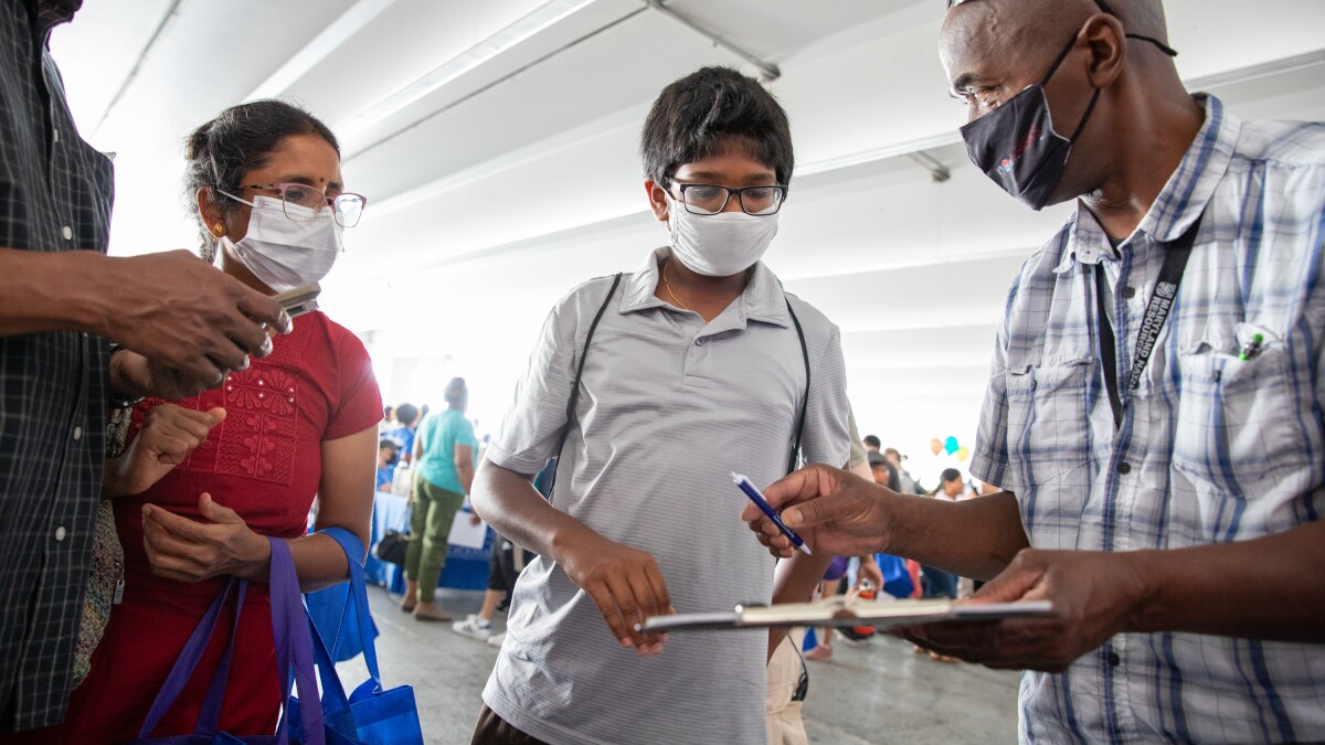 Suseela Kandasamy, left, watches Montgomery County Board of Elections official Ruel Michelin hand her 13-year-old son, Aadhavan Muralidharan, an application to be a student aide to poll workers in Wheaton, Md.