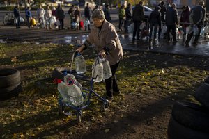 Catherine, 75, pushes her walker loaded with plastic bottles after refilling them in a tank, in the center of Mykolaiv, Monday, Oct. 24, 2022