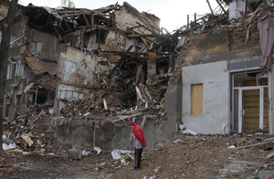 File - Local resident Nina, 72, stands near her house, ruined by the Russian shelling a month ago in central Slavyansk, Donetsk region, Ukraine, Saturday, Oct. 29, 2022. She keeps living in this house and collects wooden debris to make an outdoor fire for cooking.