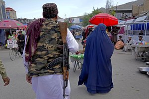 A woman wearing a burka walks through the old market as a Taliban fighter stands guard, in downtown Kabul, Afghanistan, Sunday, May 8, 2022