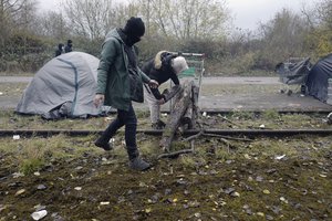 Migrants carry wood in a makeshift camp outside Calais, northern France, Saturday, Nov. 27, 2021