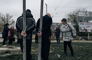 Local residents look at two alleged collaborators tied by the hands to pillars in Kherson, Ukraine, Sunday, Nov. 13, 2022.