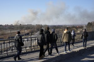 Pedestrians walk over an overpass as a cloud of smoke raises after an explosion in Lviv, Western Ukraine, Friday, March 18, 2022