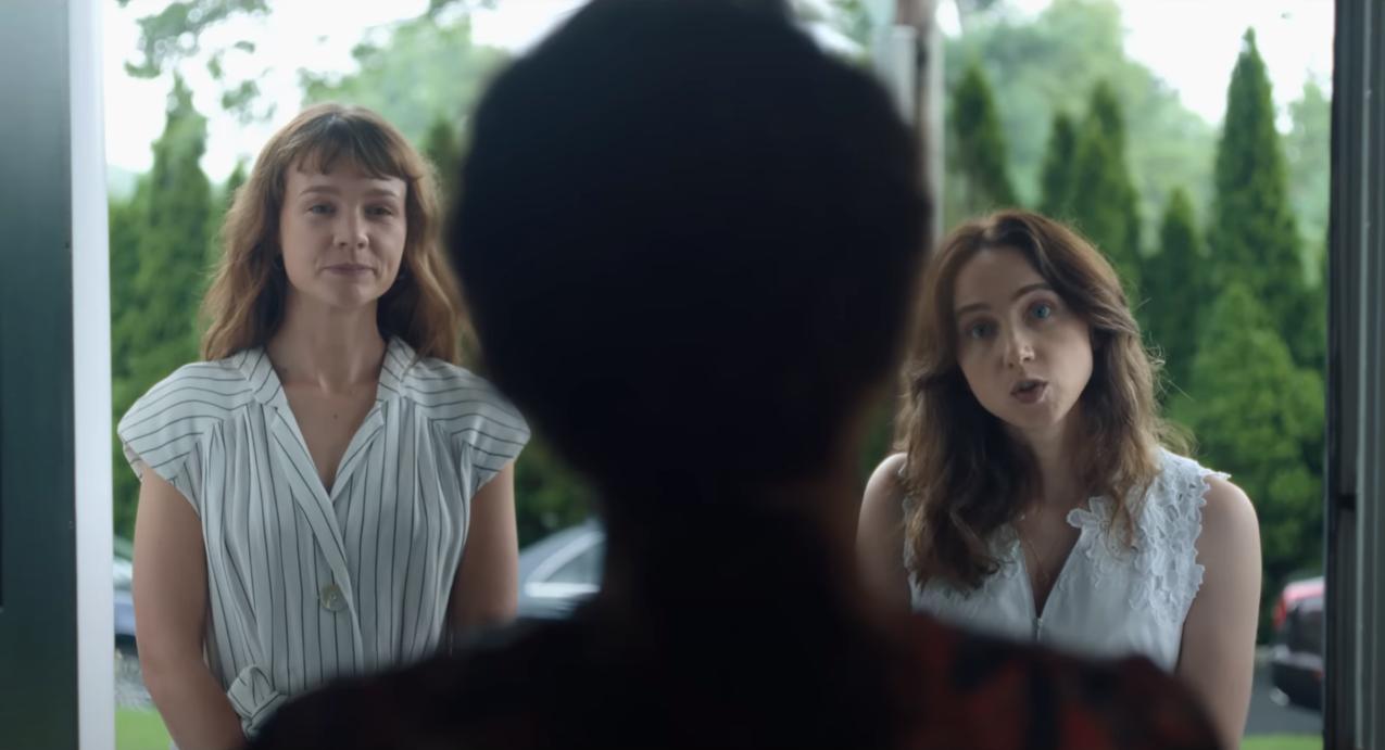 Two women stand on a doorstep, a head silhouetted in front of them.