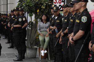 A currency exchange shop worker, seated at center, awaits clients, surrounded by riot police in Lima, Peru, Wednesday, Dec. 14, 2022.