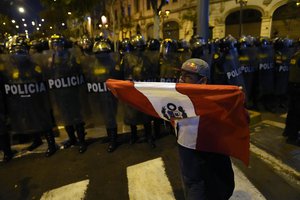 A supporter of ousted Peruvian President Pedro Castillo holds a national flag in front of a cordon of riot police, in Lima, Peru, Thursday, Dec. 15, 2022