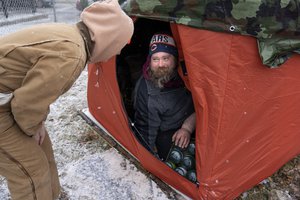 "Orange tent project" volunteer Morgan Mcluckie, left, speaks with unhoused person Peter Zielinski after giving him bottles of propane to use with his portable heater as cold and snowy weather moves in Thursday, Dec. 22, 2022, in Chicago. Officially the nonprofit "Feeding People Through Plants," founder Andy Robledo set out to find unhoused people and give them large orange tents used for ice fishing to replace other tents and shelters that are inadequate for severe winter weather.