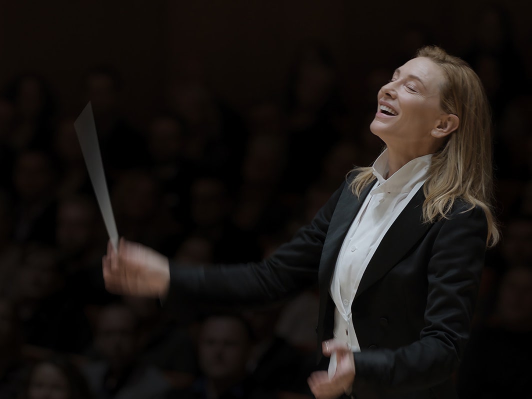 Conductor Lydia Tr as portrayed by Cate Blanchett holding a baton and looking joyful.