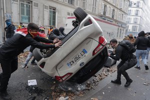 Demonstrators turn a car over during a protest against the recent shooting at the Kurdish culture center in Paris, Saturday, Dec. 24, 2022.