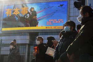 Residents wearing face masks wait to cross a traffic intersection near a large screen promoting the Chinese People's Liberation Army Airforce, in Beijing, Monday, Jan. 9, 2023.