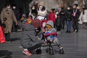 A woman feeds snack food to a child on a stroller at Qianmen pedestrian shopping street, a popular tourist spot in Beijing, Tuesday, Jan. 17, 2023.