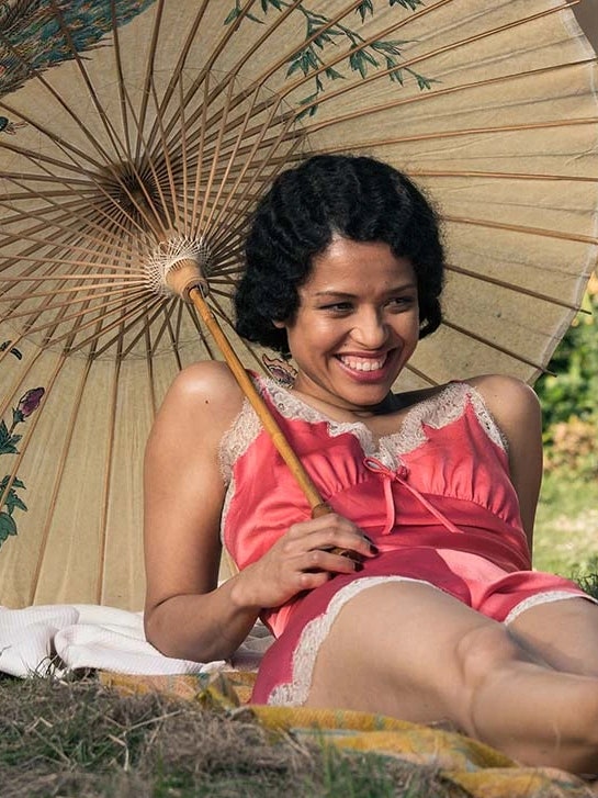 Two women under an umbrella lying on a meadow in ‘Summerland.