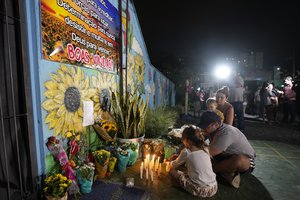 A family lights a candle at a makeshift memorial at the "Cantinho do Bom Pastor" daycare center after a fatal attack on children in Blumenau, Brazil, Wednesday, April 5, 2023