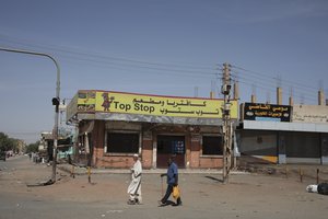 People walk past shuttered shops in Khartoum, Sudan, Tuesday, April 18, 2023