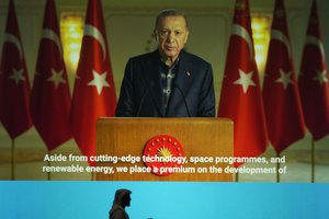 A man passes under a giant screen while Turkey's President Recep Tayyip Erdogan addresses the audience in a recorded speech