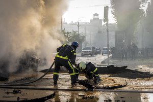 A firefighter helps his colleague to escape from a crater as they extinguish smoke from a burned car after a Russian attack in Kyiv, Ukraine, Monday, Oct. 10, 2022