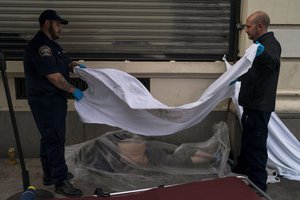 FILE - Forensic assistant Laurentiu Bigu, left, and investigator Ryan Parraz from the Los Angeles County coroner's office cover the body of a homeless man found dead on a sidewalk in Los Angeles on April 18, 2022.