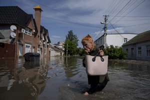 A local resident makes her way through a flooded road after the walls of the Kakhovka dam collapsed overnight, in Kherson, Ukraine, Tuesday, Jun 6, 2023.