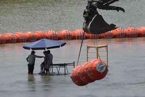 Workers take a break from deploying large buoys to be used as a border barrier along the banks of the Rio Grande in Eagle Pass, Texas, Wednesday, July 12, 2023.