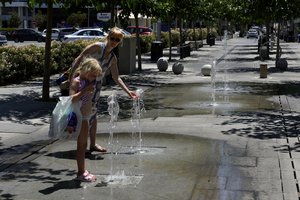 A mother with her child get some coolness from a fountain in downtown capital Nicosia, Cyprus, on Friday, July 14, 2023