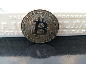 Bitcoin solid coin leaning on a white strip with engraved words.