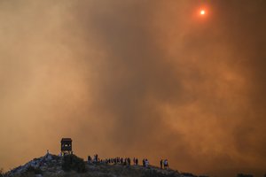 People watch the fire in Mandra west of Athens, on Tuesday, July 18, 2023. In Greece, where a second heatwave is expected to hit Thursday, three large wildfires burned outside Athens for a second day. Thousands of people evacuated from coastal areas south of the capital returned to their homes Tuesday when a fire finally receded after they spent the night on beaches, hotels and public facilities.