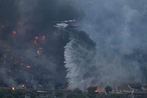 A firefighting helicopter dumps water as fire approaches houses in Kalamaki near Agioi Theodori about 60 kilometers west of Athens, Monday, July 17, 2023