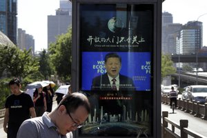 People walk by an electronic display panel advertising a video footage of Chinese President Xi Jinping speaking at the World Economy Forum on a street in Beijing, Wednesday, May 30, 2018.