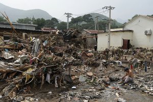 A man washes his clothes in a stream near debris left over after flood waters devastate the village of Nanxinfang village on the outskirts of Beijing, Friday, Aug. 4, 2023