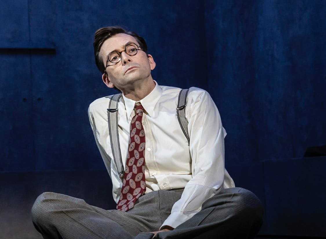 GOOD show image. A man in a white shirt and tie sits cross-legged on the floor.