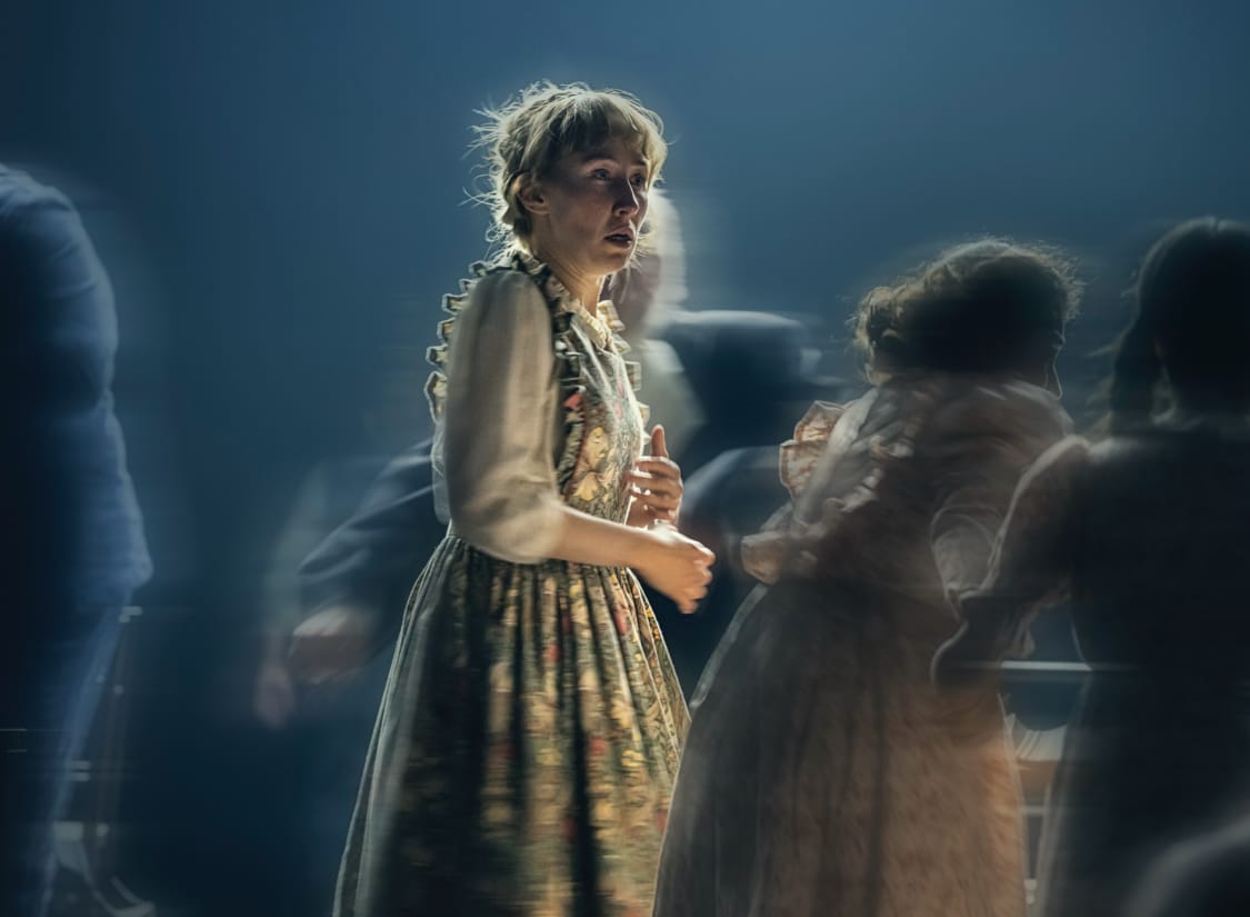 The Crucible show image. A photograph taken from the floor looking up at five female faces against a white sky.