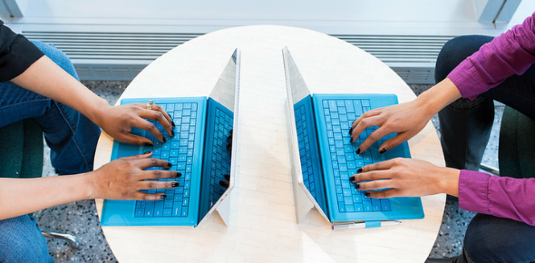 Aerial view of two pairs of hands typing at two laptops