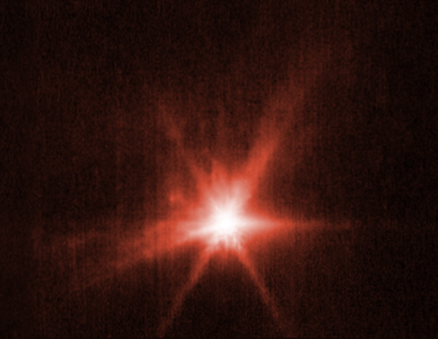 View of Didymos-Dimorphos asteroid system after DART impact. Webb's view, hued in red, shows a bright center and darker streaks emanating outward from it.